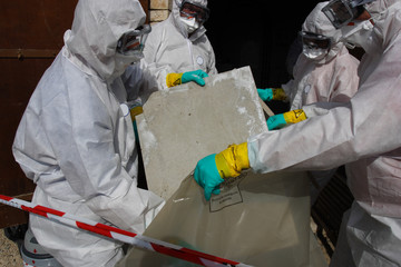 people in PPE dismantling a wall containing asbestos for disposal